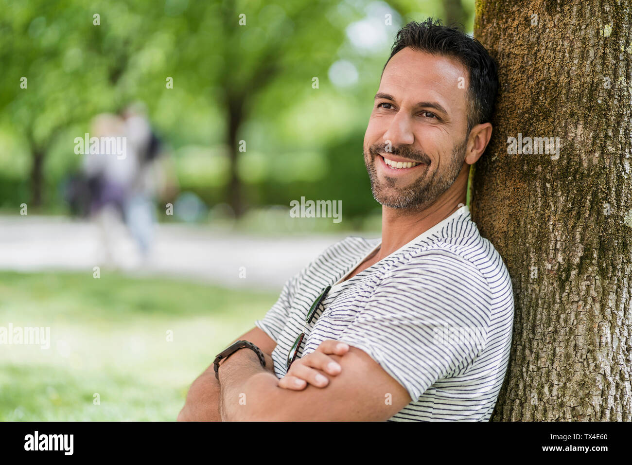 Portrait of smiling man leaning against a tree in park Banque D'Images
