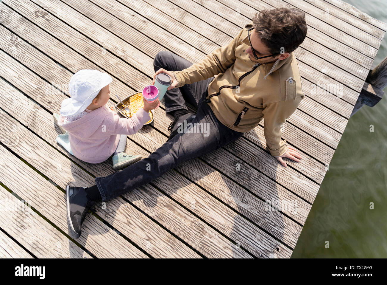Allemagne, Bavière, Ostfildern, père et fille se détendre sur jetty ayant un snack Banque D'Images