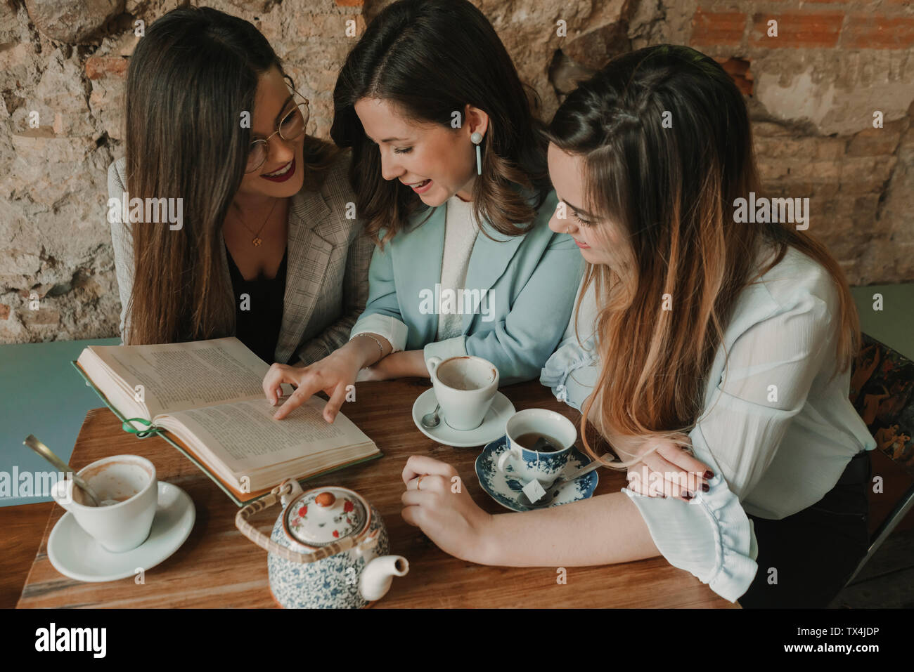 Trois jeunes femmes de la lecture d'un livre dans un café Banque D'Images