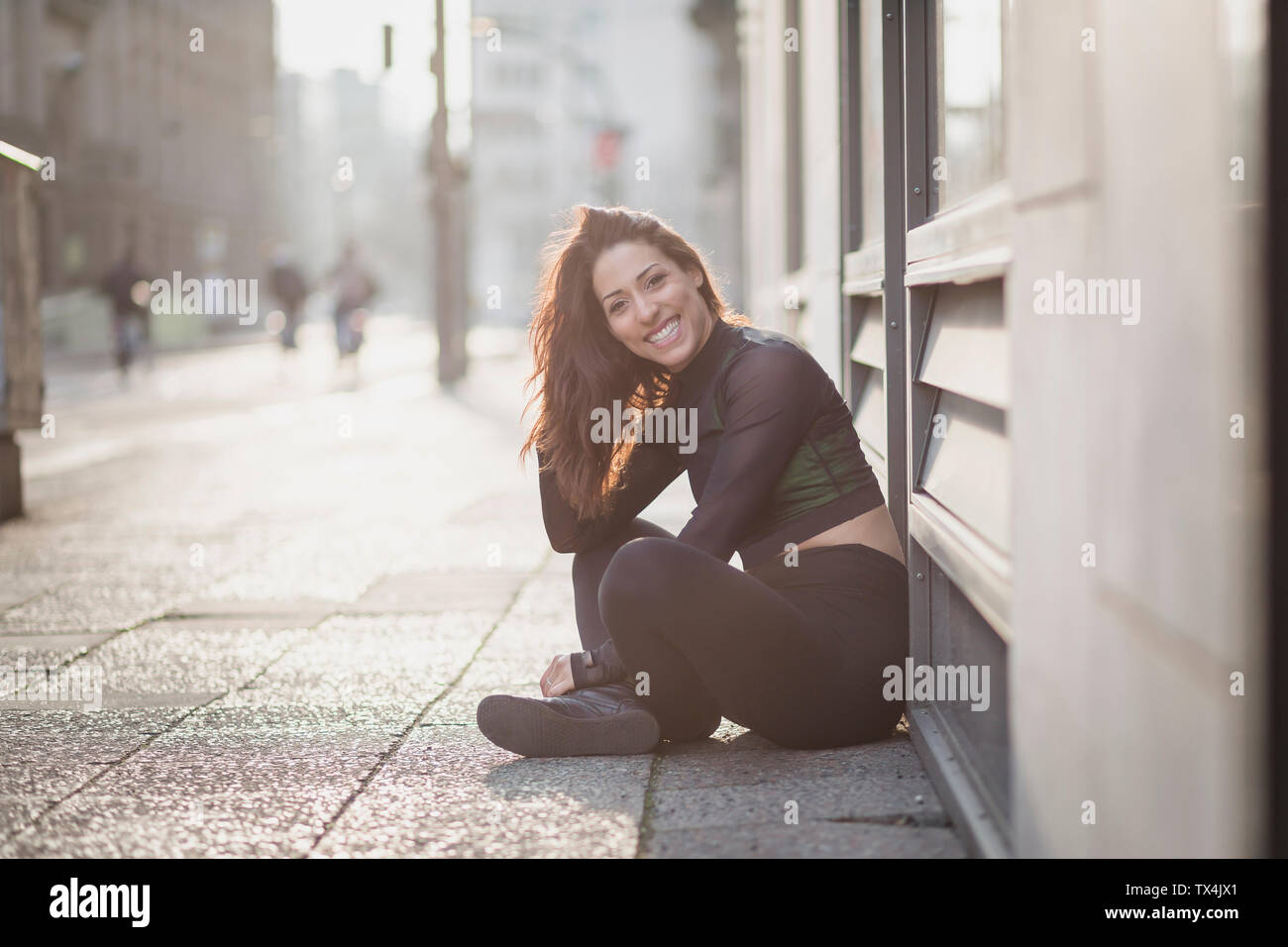Portrait of happy sportive jeune femme assise sur le sol dans la ville Banque D'Images