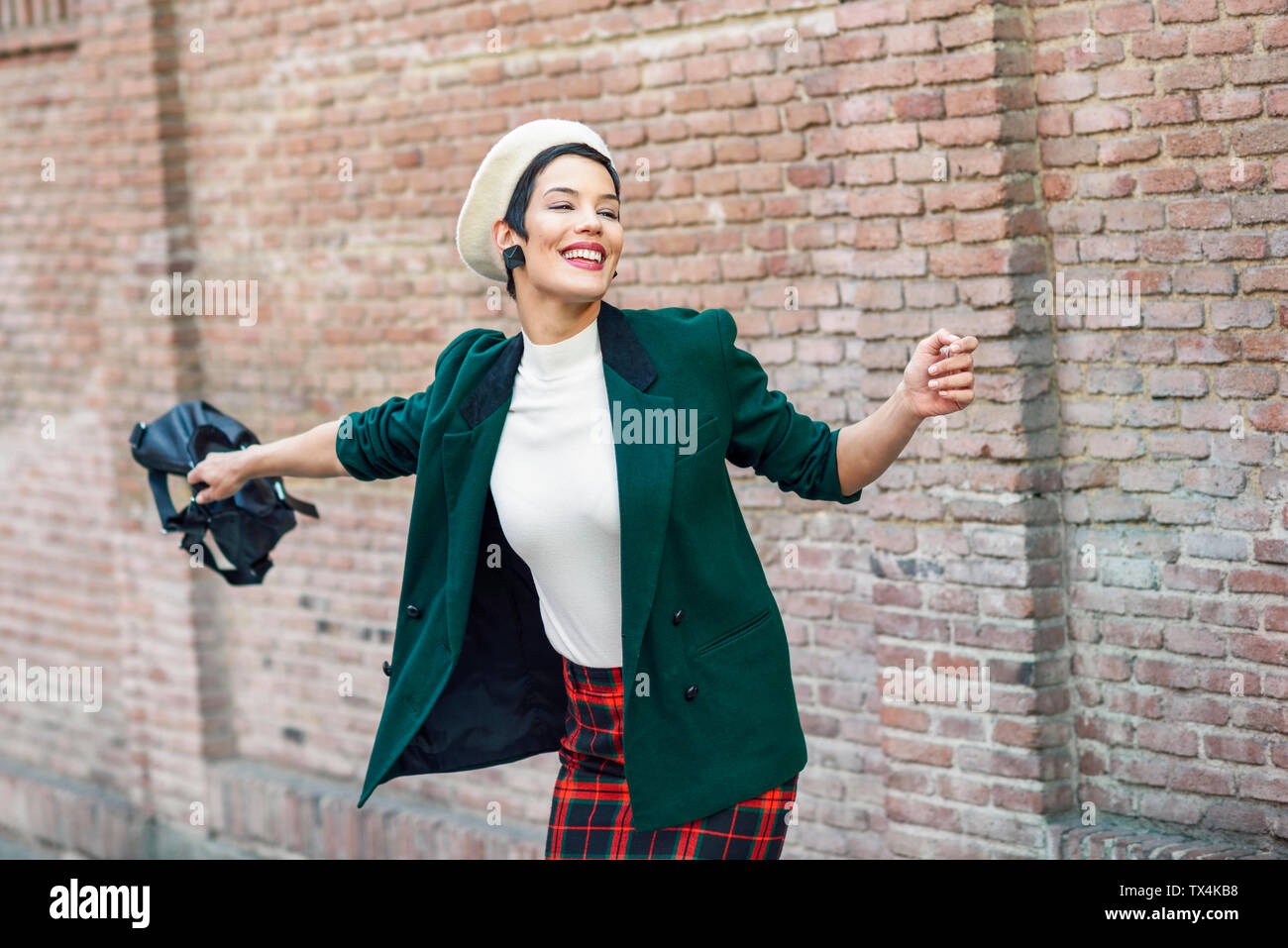 Heureux à la mode jeune femme portant un béret et une veste verte à un mur de briques Banque D'Images