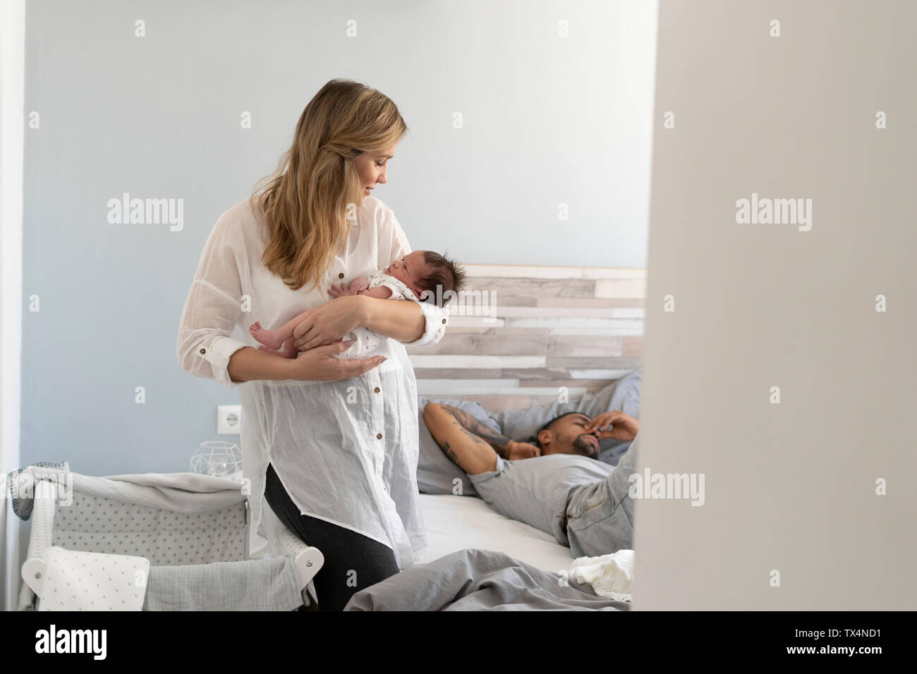 Mère tenant son nouveau-né dans la chambre à coucher avec le père en arrière-plan Banque D'Images