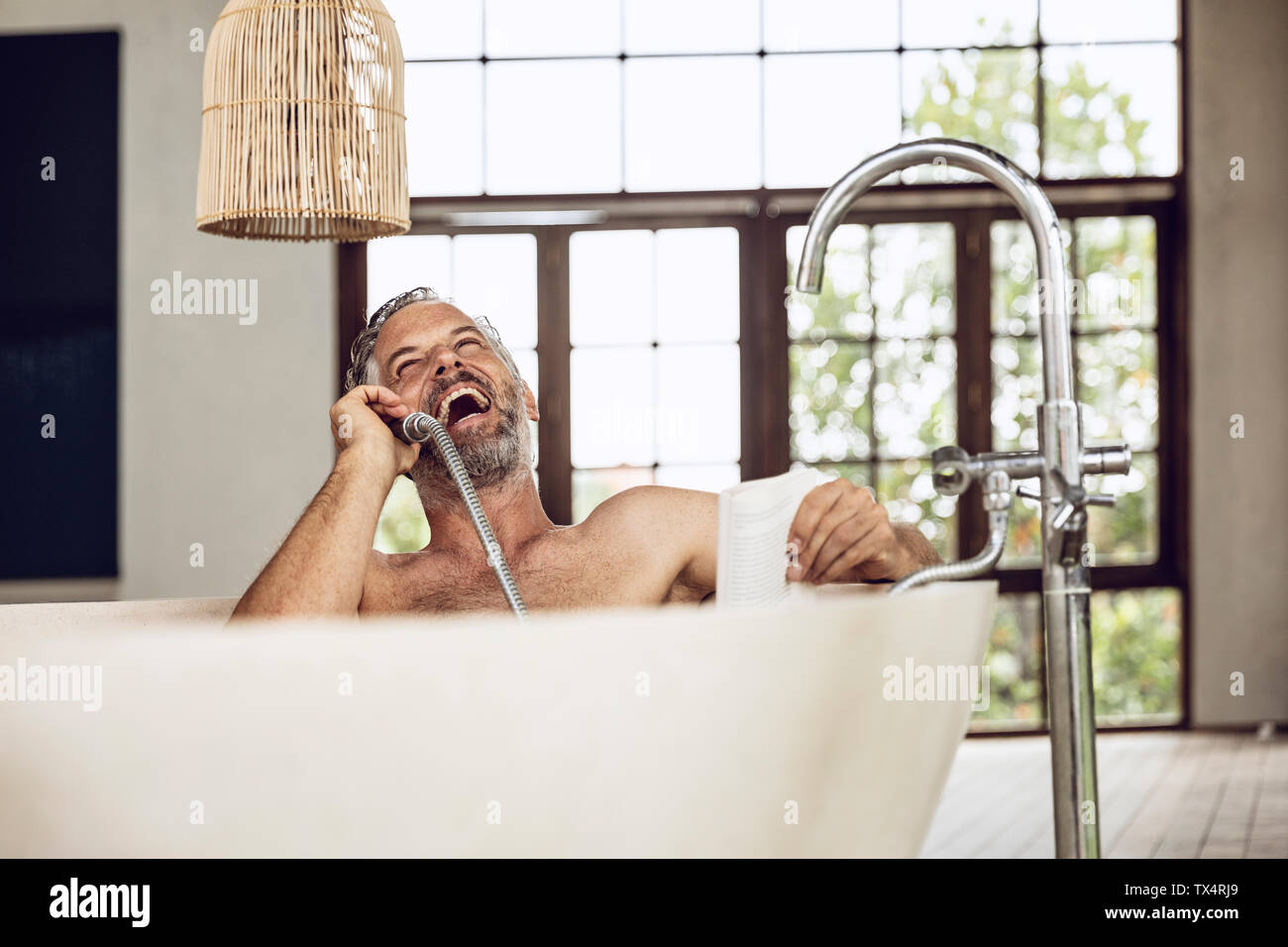 Laughing man à l'aide d'une baignoire douche tête comme récepteur du téléphone Banque D'Images