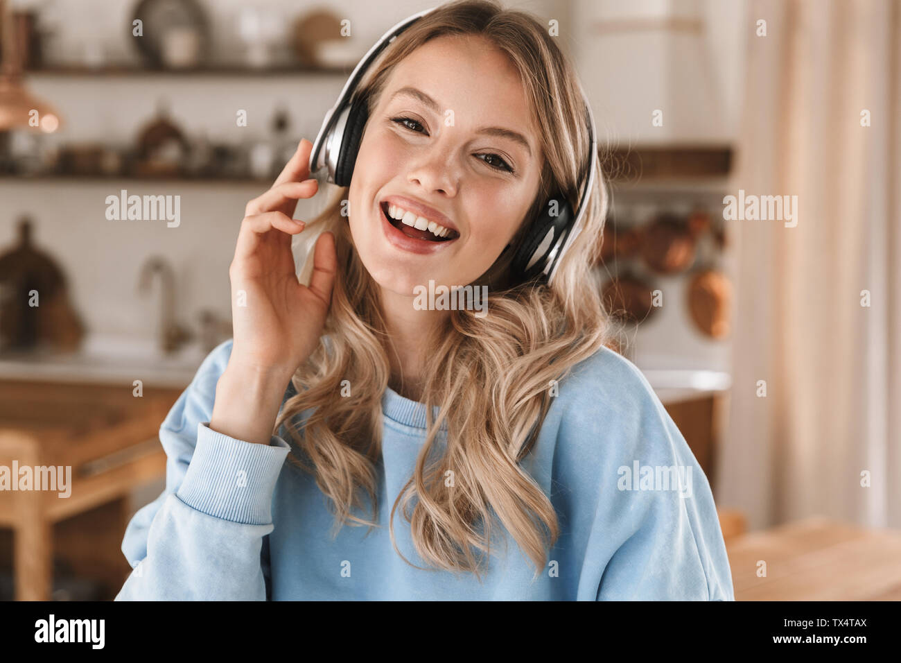 Portrait de jeune fille blonde européenne 20s portant des écouteurs de sourire et de joie tout en écoutant de la musique à la maison Banque D'Images
