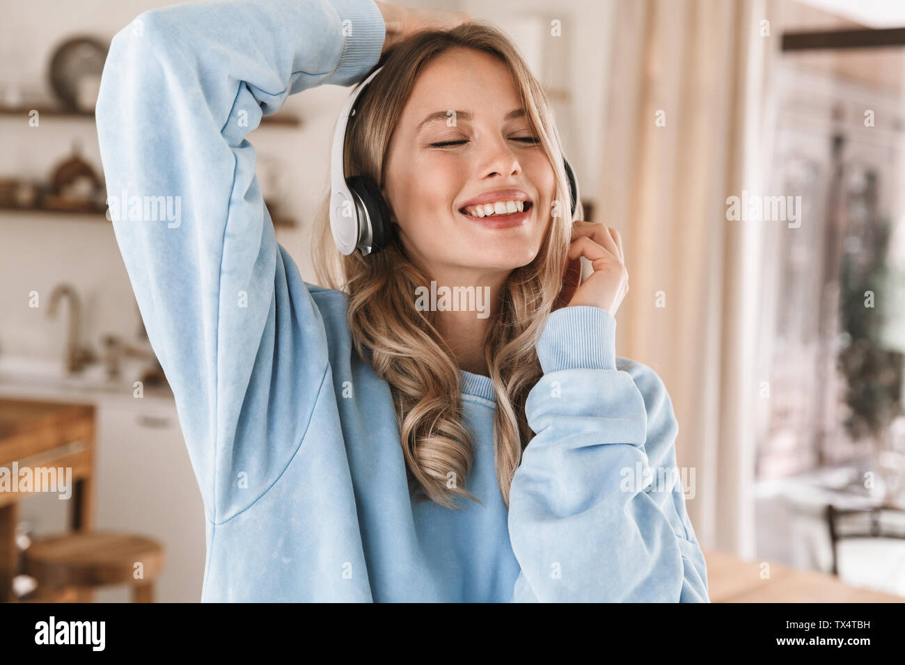 Portrait de belle fille blonde 20s portant des écouteurs de sourire et de joie tout en écoutant de la musique à la maison Banque D'Images