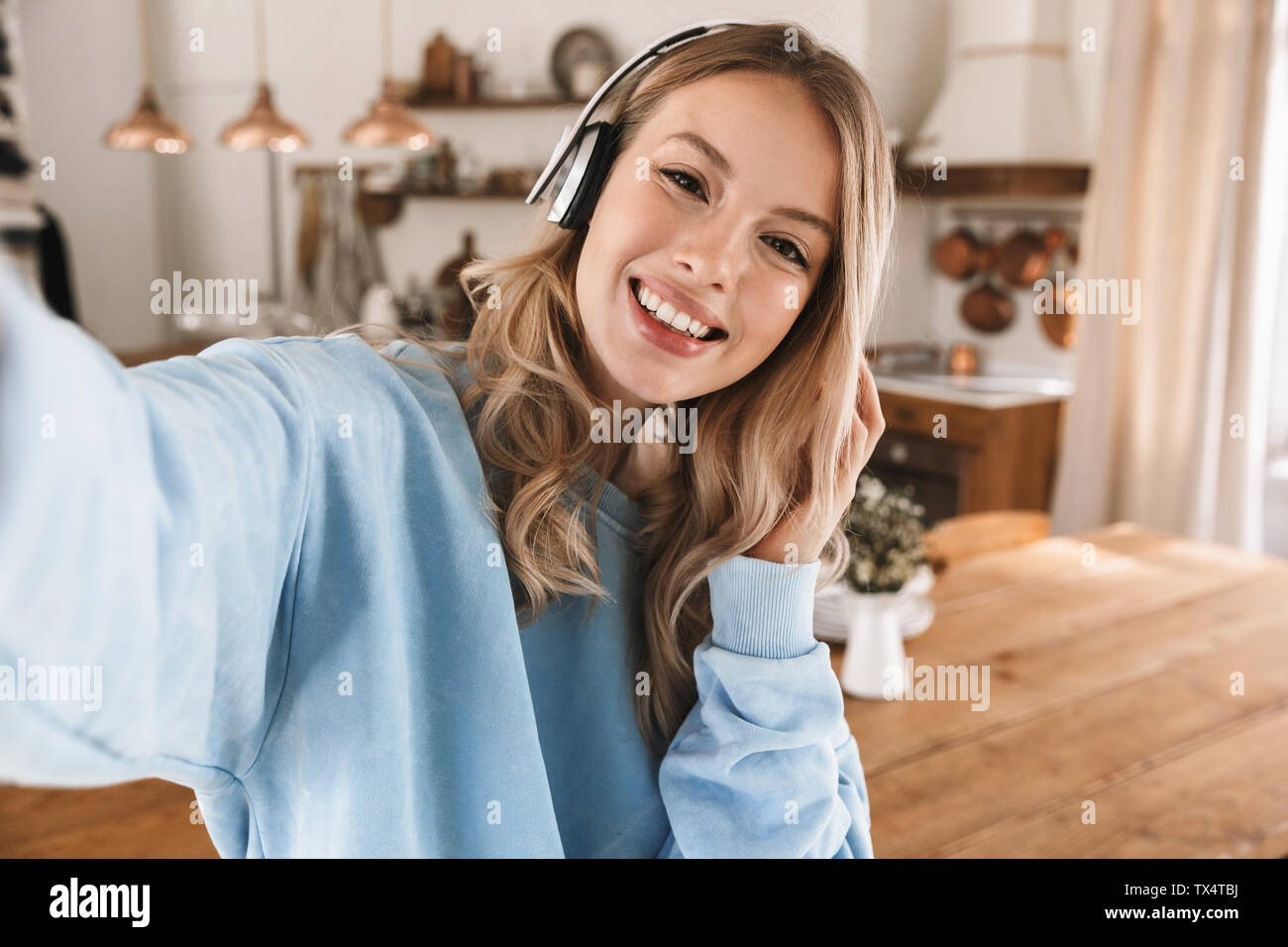 Portrait de jeune fille blonde heureux 20s portant des écouteurs de sourire et de prendre photo selfies lors de l'écoute de musique à la maison Banque D'Images