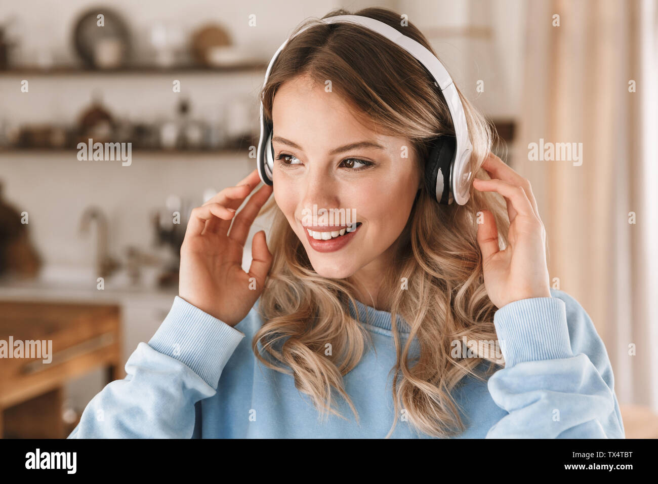 Portrait de jeune fille blonde joyeuse 20s portant des écouteurs de sourire et de joie tout en écoutant de la musique à la maison Banque D'Images