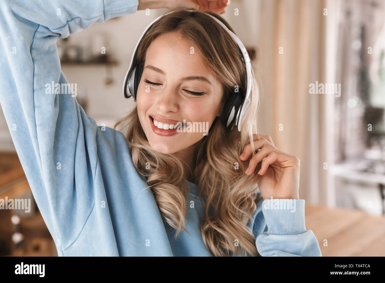 Portrait de très jolie jeune femme de 20 ans portant des écouteurs de sourire et de joie tout en écoutant de la musique à la maison Banque D'Images