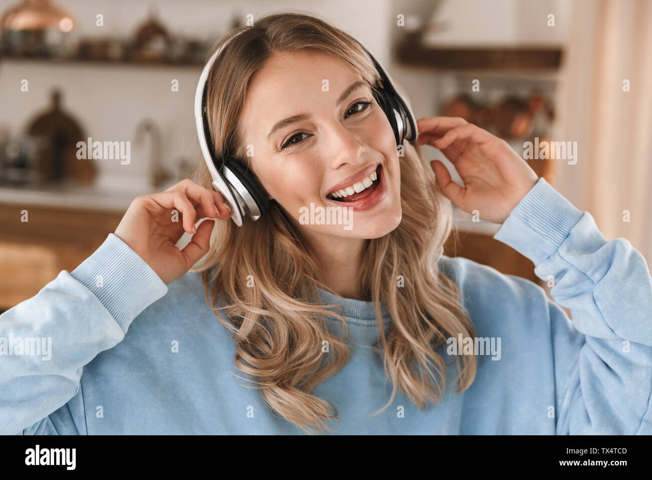 Portrait de jeune fille blonde joyeuse 20s portant des écouteurs de sourire et de joie tout en écoutant de la musique à la maison Banque D'Images