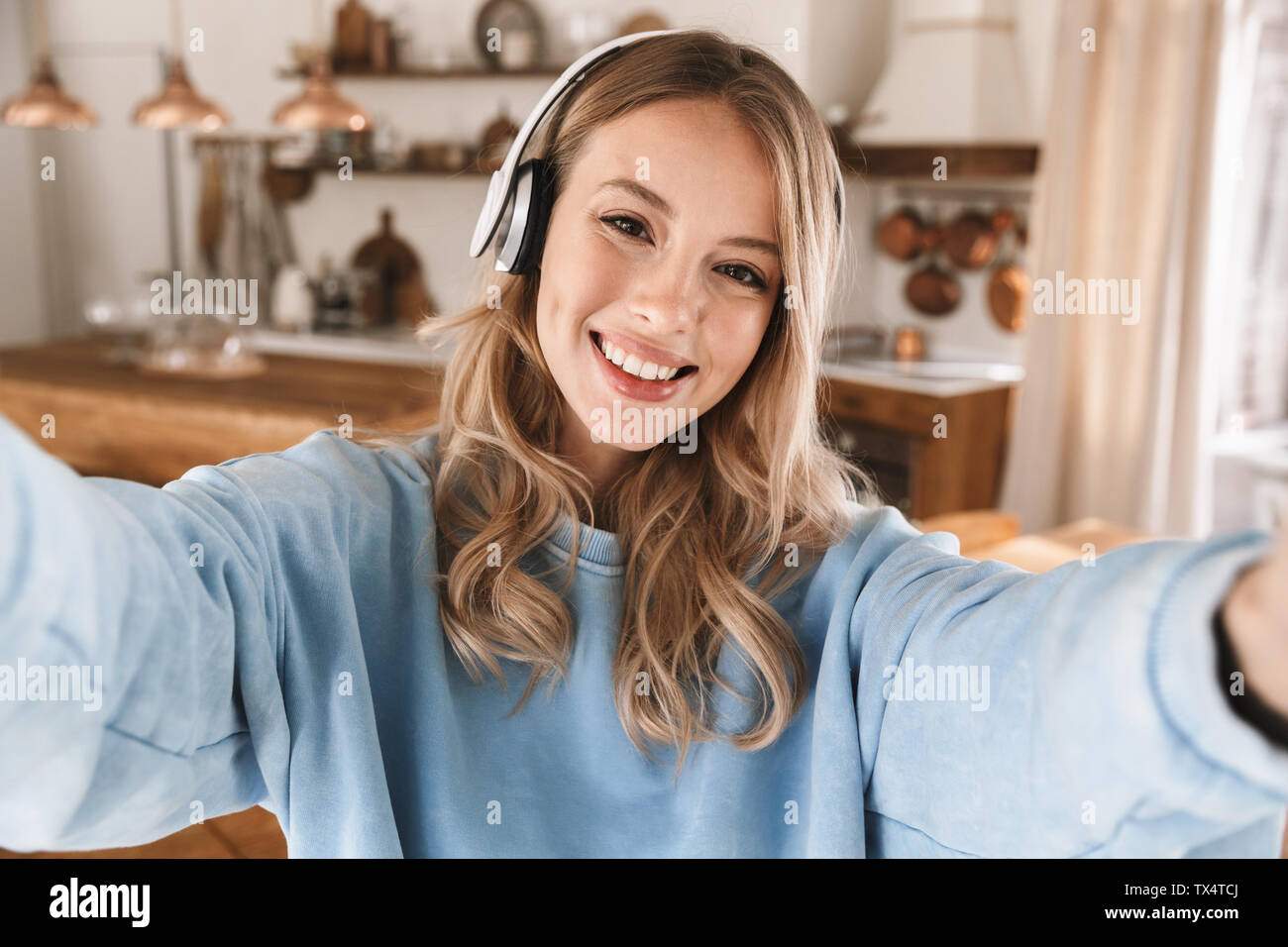 Portrait de jeune fille blonde joyeuse 20s portant des écouteurs de sourire et de prendre photo selfies lors de l'écoute de musique à la maison Banque D'Images