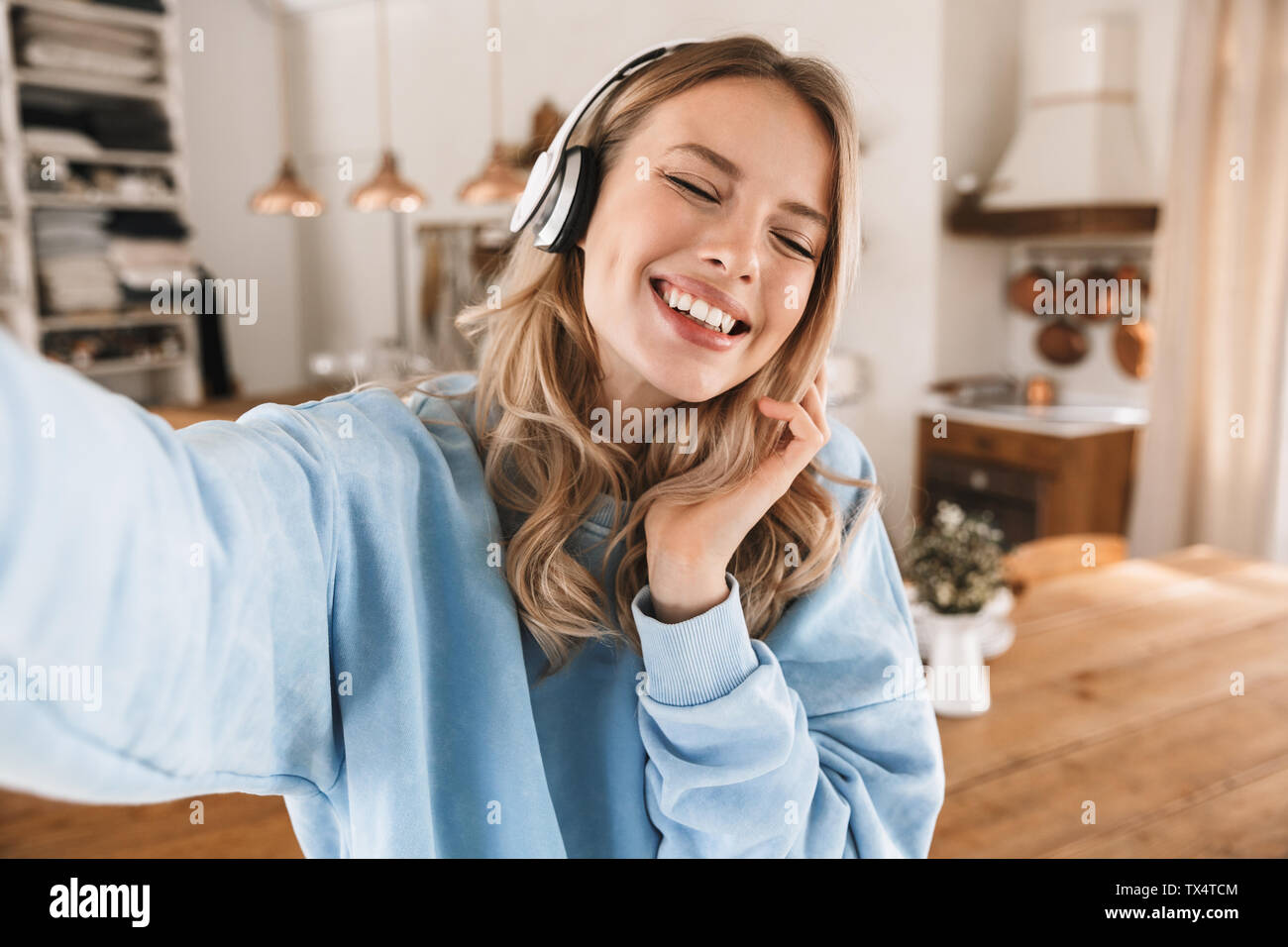 Portrait de jeune fille blonde 20s portant des écouteurs de sourire et de prendre photo selfies lors de l'écoute de musique à la maison Banque D'Images