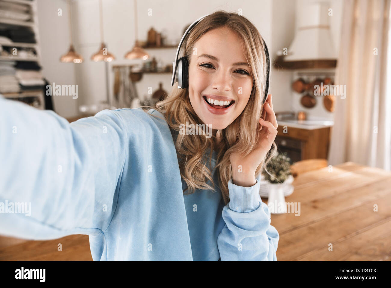 Portrait of attractive blonde girl 20s portant des écouteurs de sourire et de prendre photo selfies lors de l'écoute de musique à la maison Banque D'Images