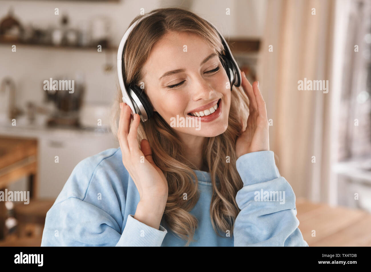 Portrait of gorgeous blonde girl 20s portant des écouteurs de sourire et de joie tout en écoutant de la musique à la maison Banque D'Images