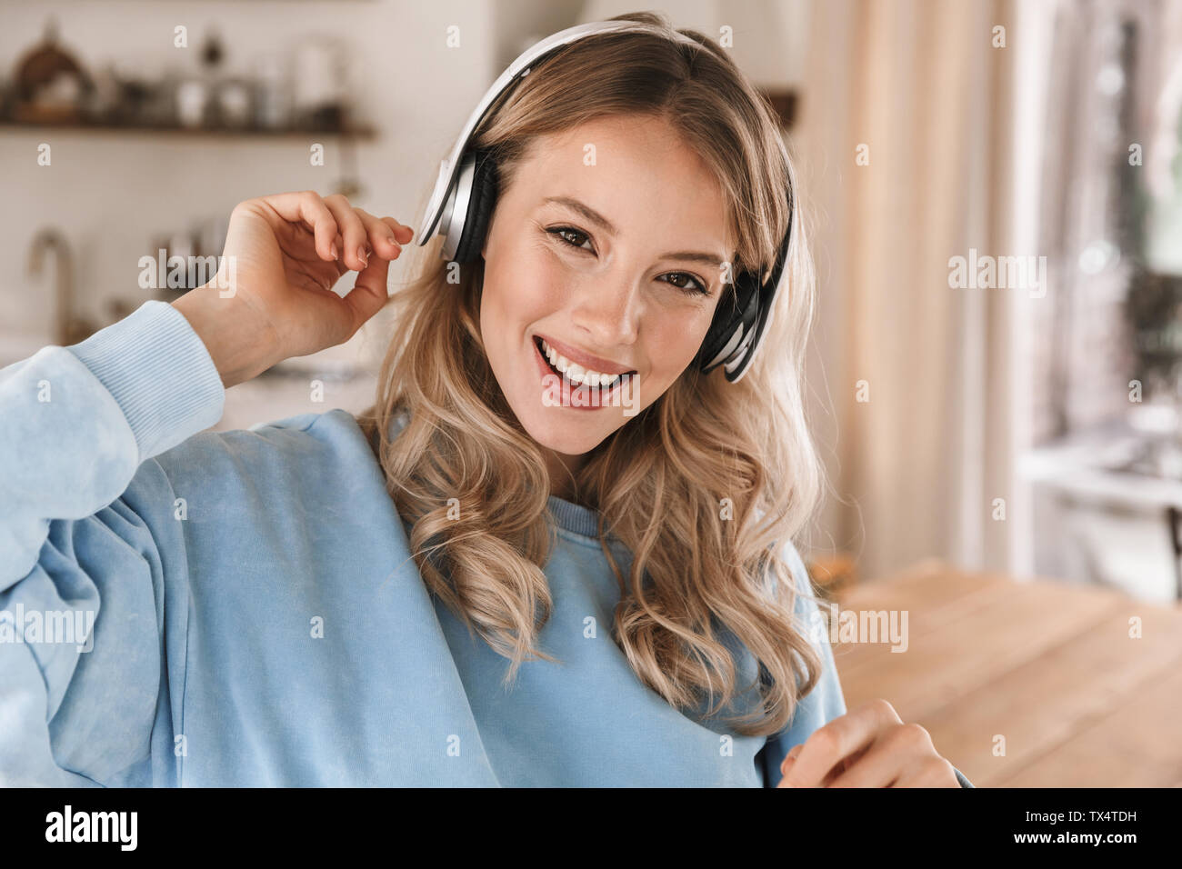 Portrait de charmante blonde girl 20s portant des écouteurs de sourire et de joie tout en écoutant de la musique à la maison Banque D'Images