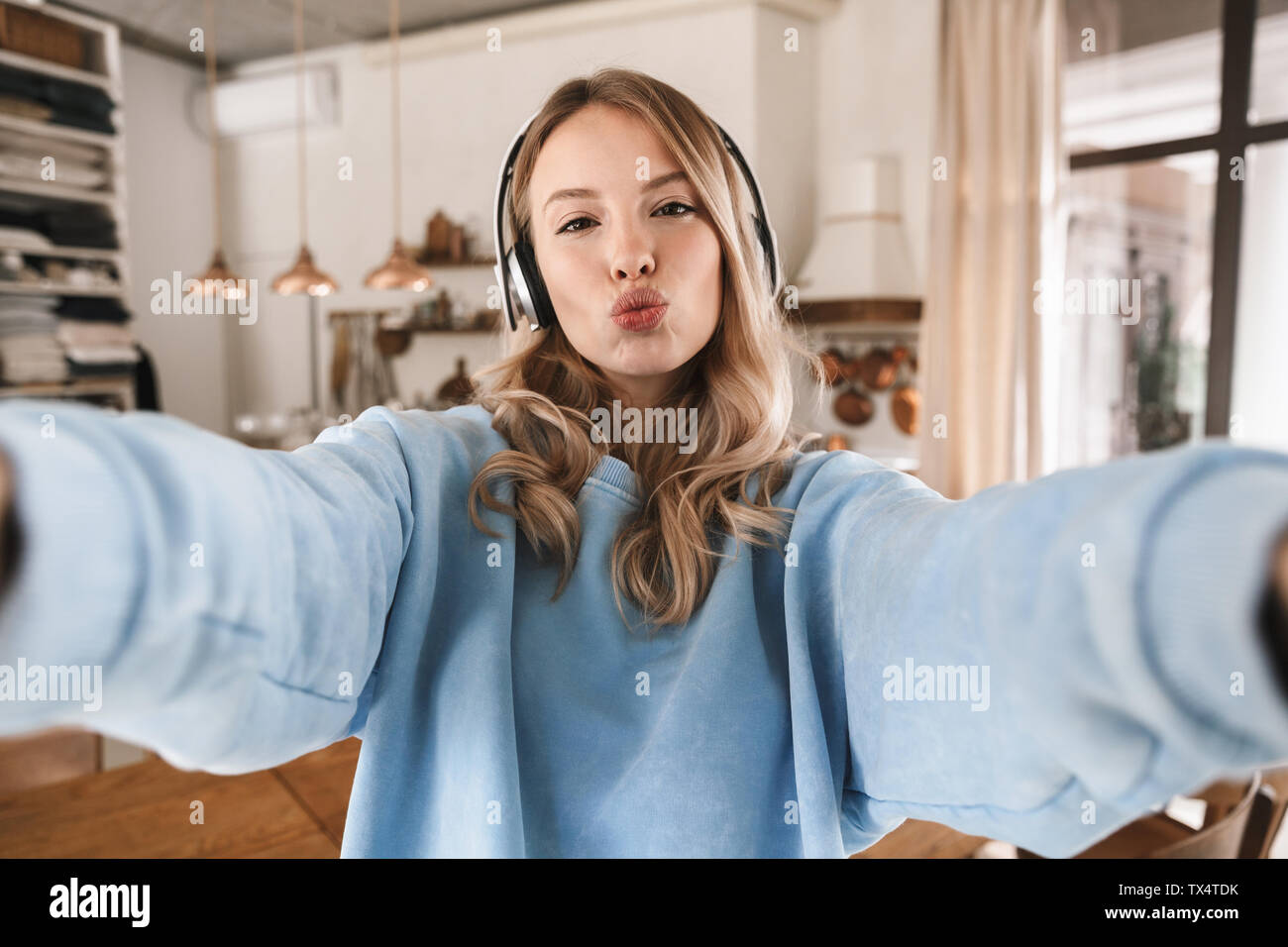 Portrait de belle fille blonde 20s portant des écouteurs de sourire et de prendre photo selfies lors de l'écoute de musique à la maison Banque D'Images