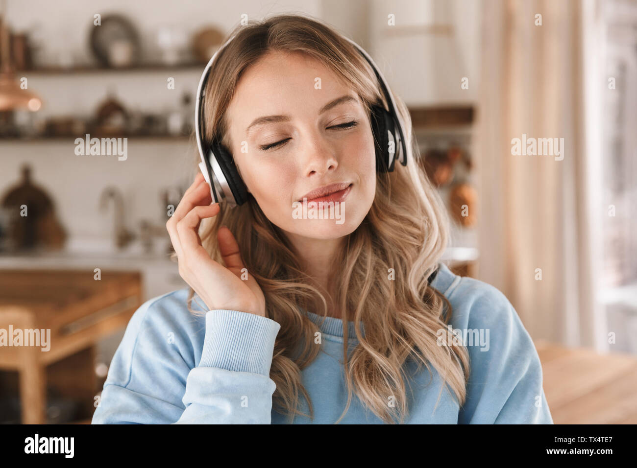 Portrait de jeune fille blonde contenu 20s portant des écouteurs de sourire et de joie tout en écoutant de la musique à la maison Banque D'Images