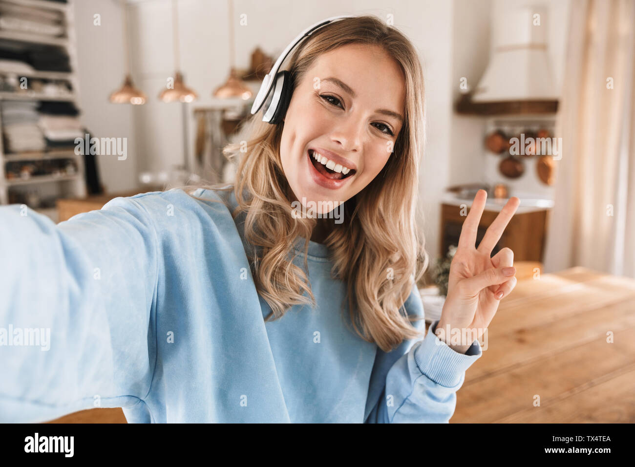 Portrait de jeune fille blonde satisfait 20s portant des écouteurs de sourire et de prendre photo selfies lors de l'écoute de musique à la maison Banque D'Images