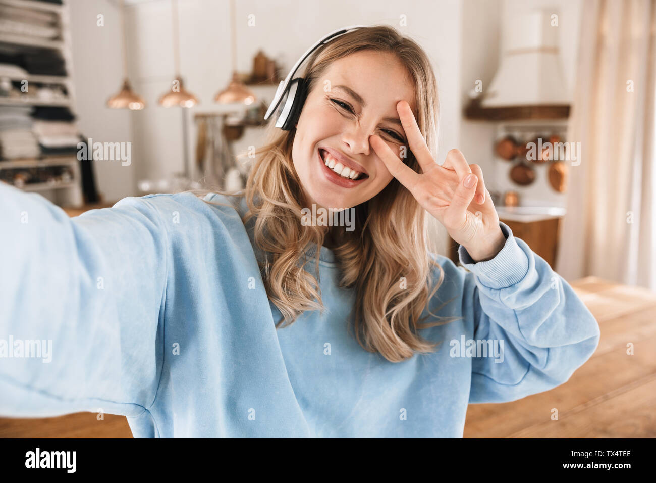 Portrait of caucasian blonde 20s portant des écouteurs de sourire et de prendre photo selfies lors de l'écoute de musique à la maison Banque D'Images