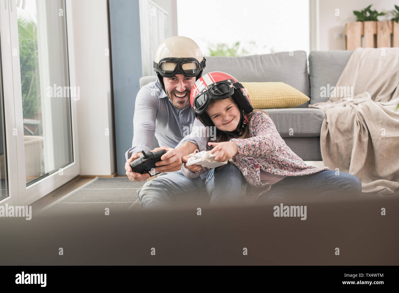 Jeune homme et petite fille portant des casques de motards, jouer au jeu de course avec une console de jeux Banque D'Images
