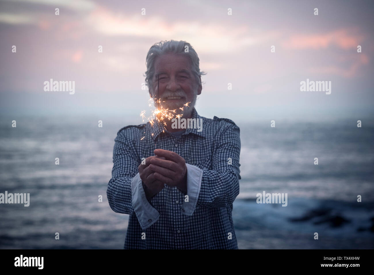 Happy senior man standing in front of the sea par sunset holding sparkler Banque D'Images