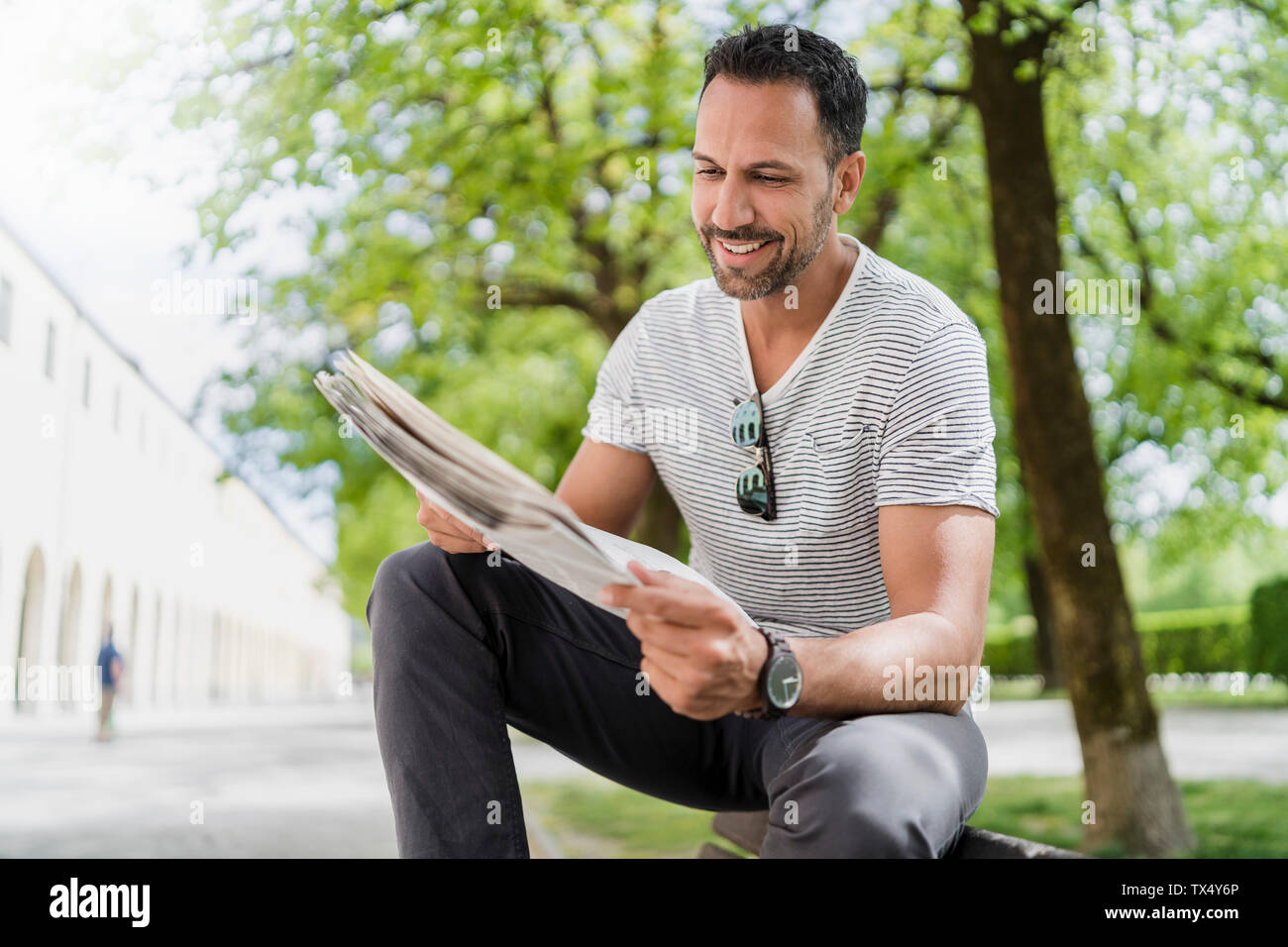 Smiling man sitting on park bench reading newspaper Banque D'Images