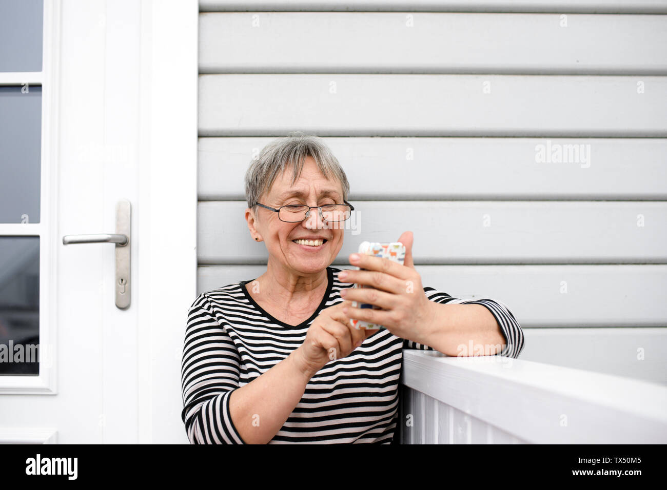 Happy senior woman using cell phone sur le porche de sa maison Banque D'Images