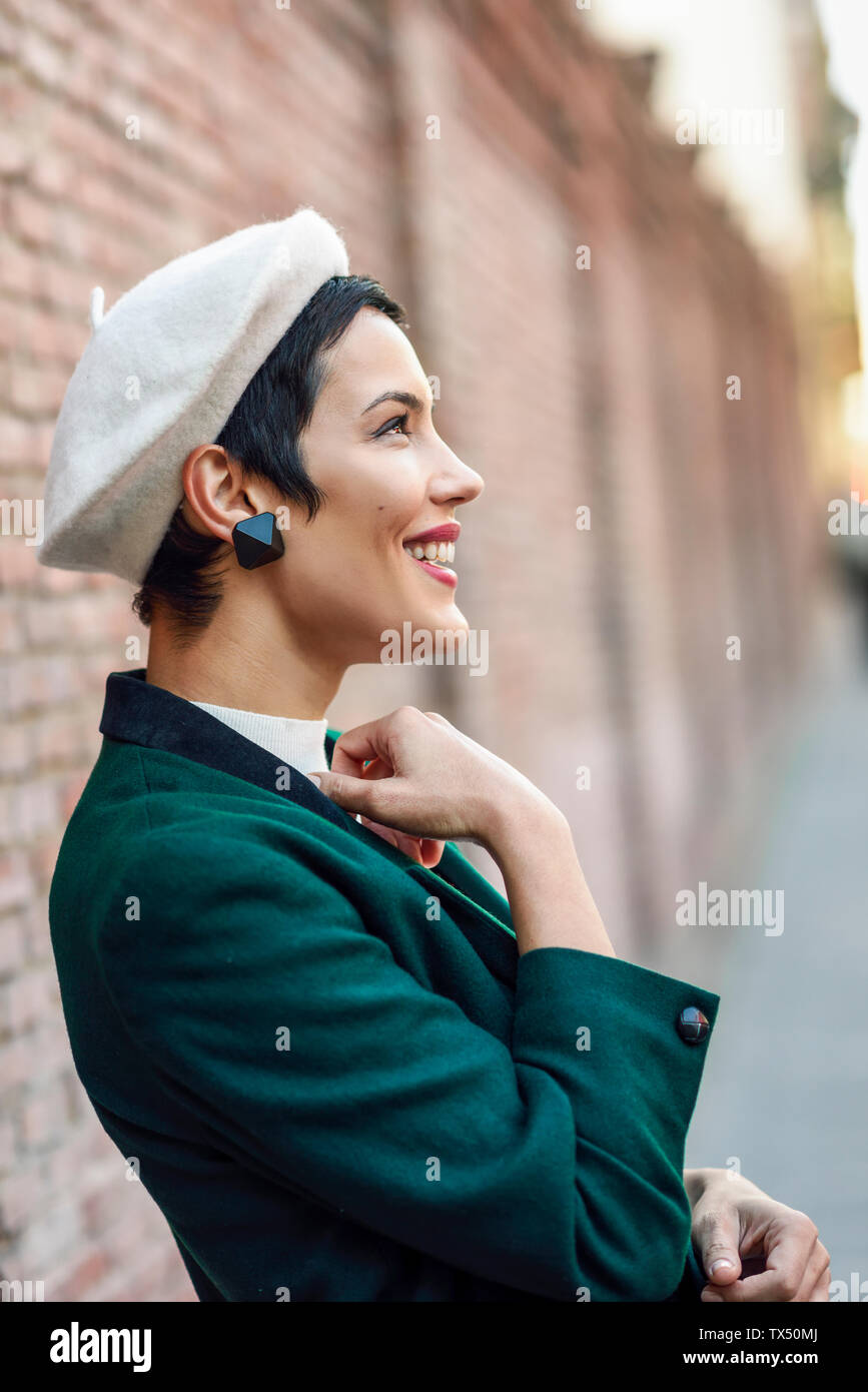 Heureux à la mode jeune femme portant un béret et une veste verte à un mur de briques Banque D'Images