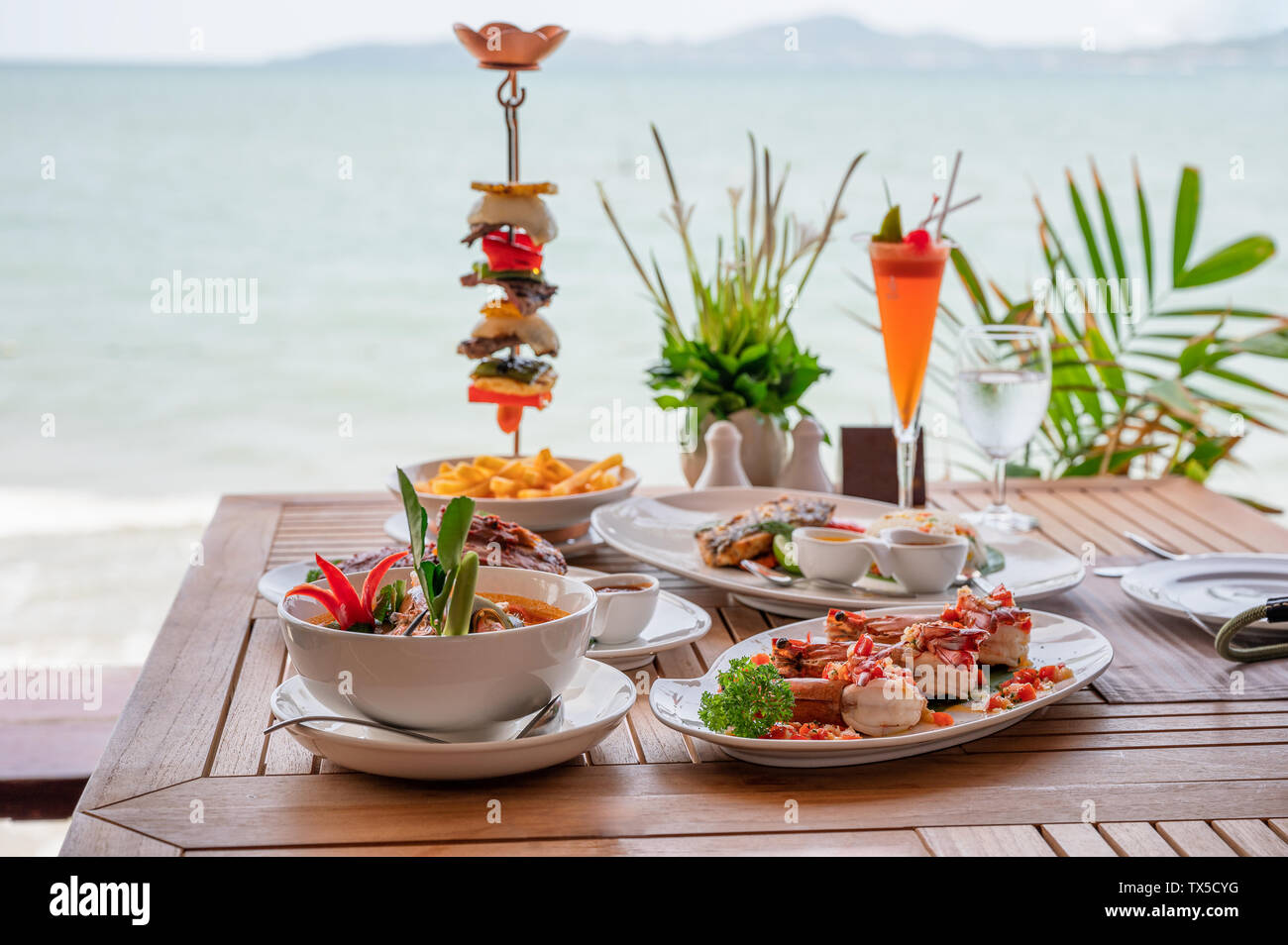 Variété d'aliments, des côtes de porc rôti, steak de boeuf, fruits de mer et soupe épicée sur table à manger en mer tropicale Banque D'Images