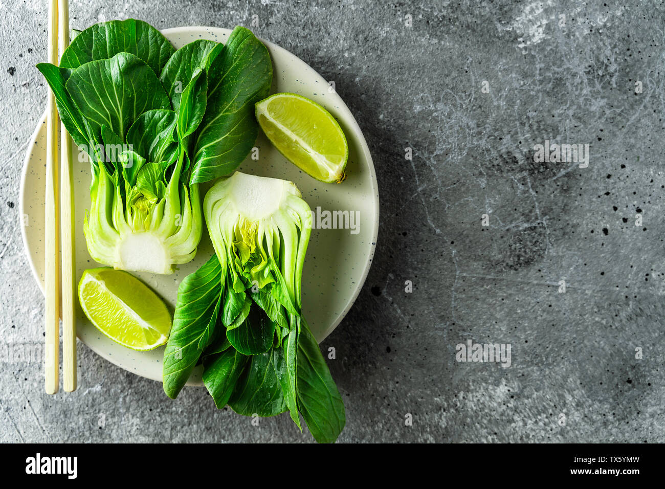 Le Bok choy, les moitiés de tranches de lime, baguettes sur plaque blanche sur fond gris. Top View with copy space Banque D'Images