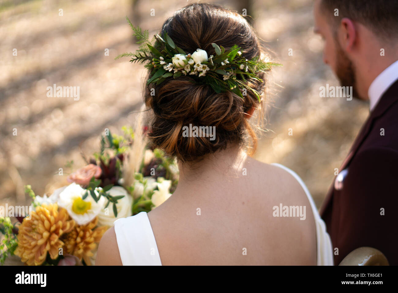 Arrière de la tête et de la vue latérale d'une mariée, fleurs dans les cheveux avec son mari et bouquet dans l'arrière-plan. Banque D'Images