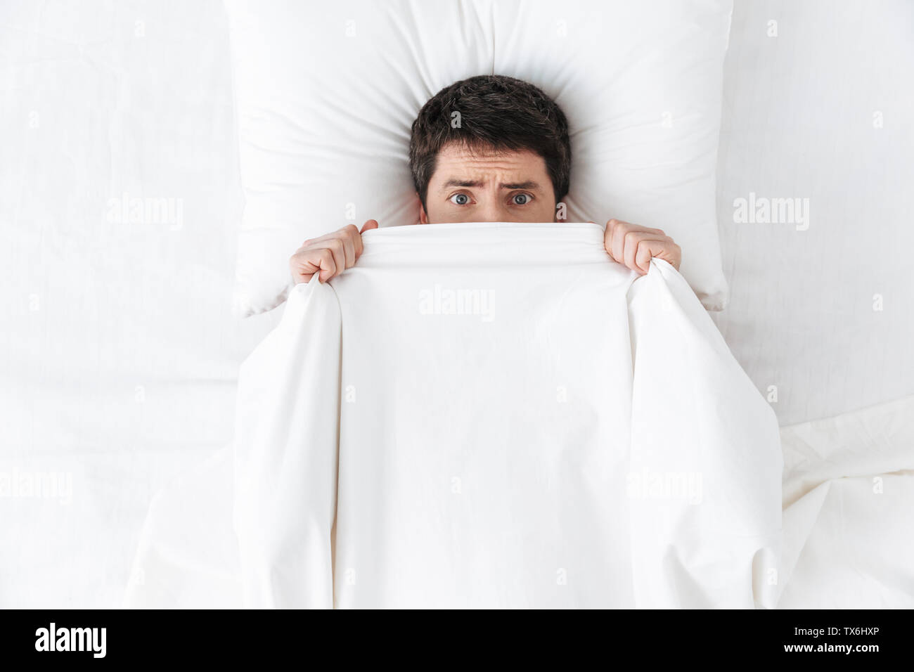 Image d'un beau jeune homme dans la matinée sous couverture Masquer au lit. Banque D'Images