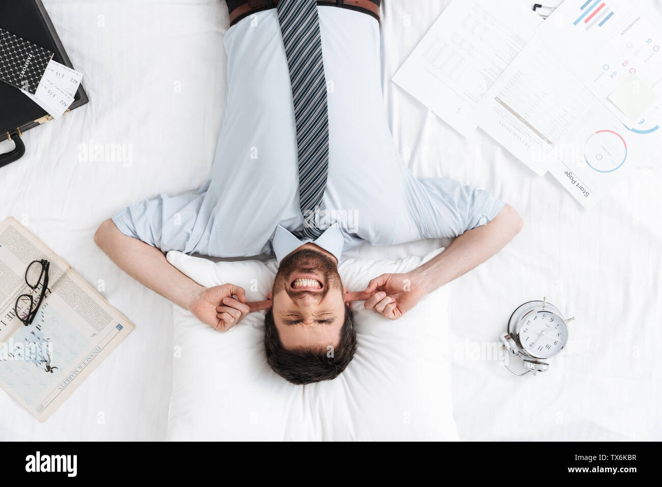 Vue de dessus d'un agacé businessman wearing shirt laying in bed, travailler tard, cris Banque D'Images