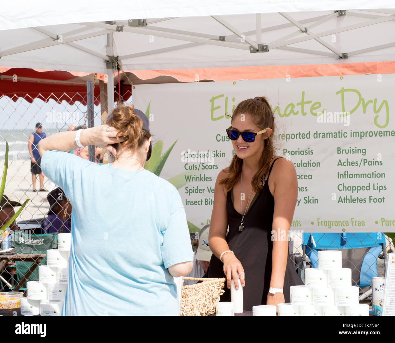 Une jeune femme brune à lunettes vend des produits de soin de peau d'aloès à un distributeur stand. En 2019 Texas Sandfest Port Aransas, Texas USA. Banque D'Images