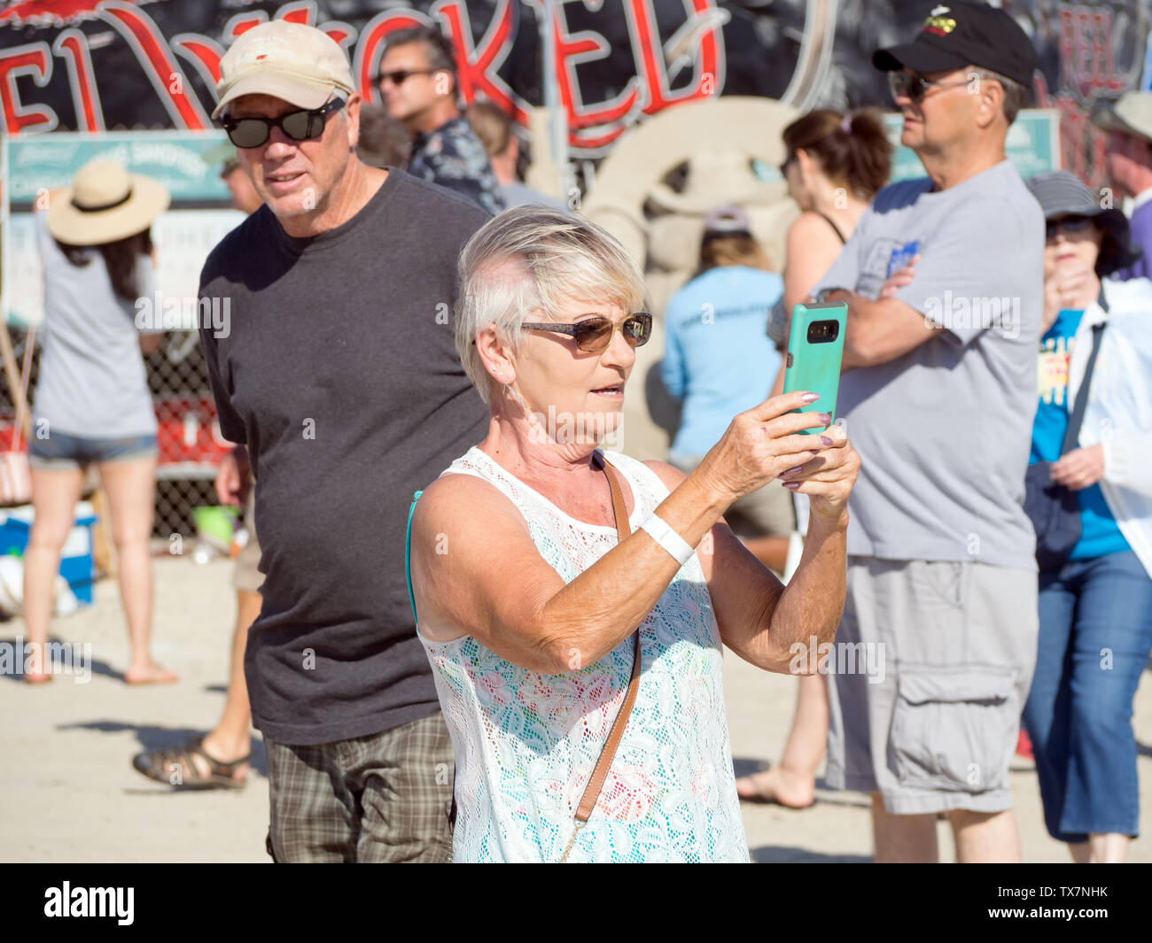A senior woman in sunglasses prend une photo avec un téléphone cellulaire à la Texas 2019 Sandfest à Port Aransas, Texas USA. Banque D'Images
