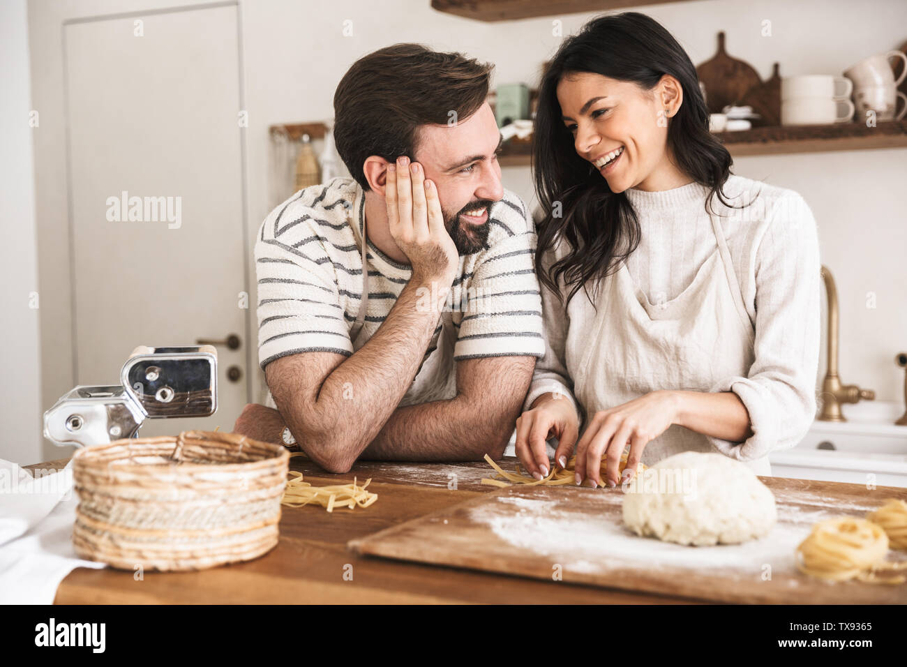 Portrait de l'homme et la femme couple positif 30s portant des tabliers des pâtes de la pâte pendant la cuisson ensemble dans la cuisine à la maison Banque D'Images