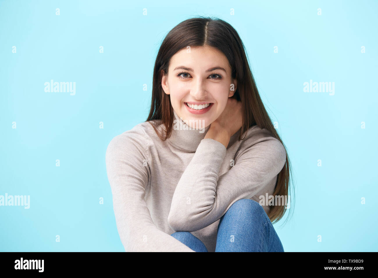 Studio portrait d'une jolie femme de race blanche, assis sur le plancher, smiling, isolé sur fond bleu Banque D'Images