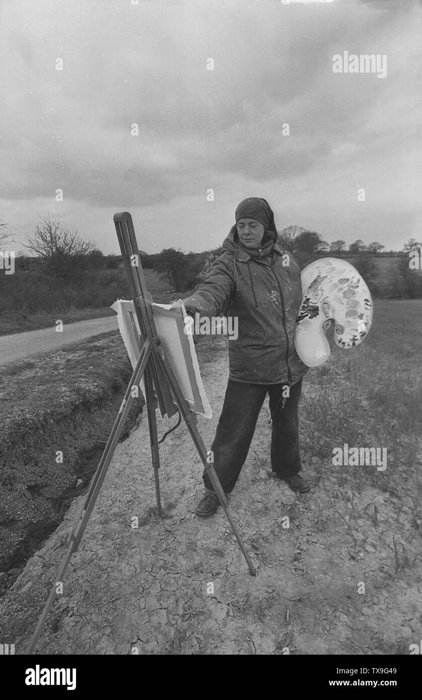 Des années 1980, à l'extérieur par une route de campagne en zone rurale et sur le bord d'un champ, une artiste féminine à l'aide d'huiles essentielles sur une palette debout et de peinture à un chevalet, Yorkshire, Angleterre. Banque D'Images