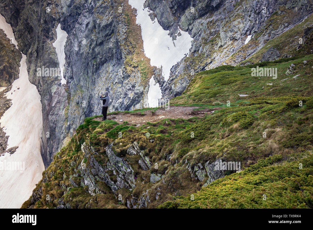 Le randonneur, la protection d'un vent avec une capuche, debout sur le bord d'une falaise sur la montagne de Rila en Bulgarie et de photographier avec son téléphone Banque D'Images