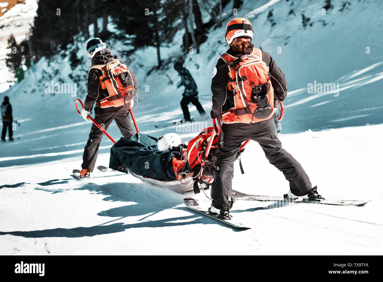 Les sauveteurs dans une station de ski d'évacuer la victime de la pente. Deux sauveteurs descendre un touriste sur une luge spécial sur une journée d'hiver ensoleillée. Blurred background Banque D'Images