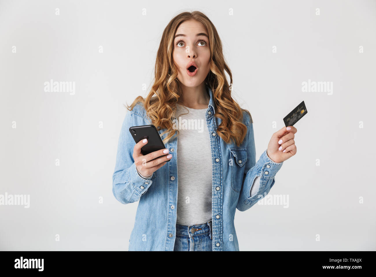 Image d'un choqué belle jeune femme assez excité posing isolated over white wall background using mobile phone holding credit card. Banque D'Images
