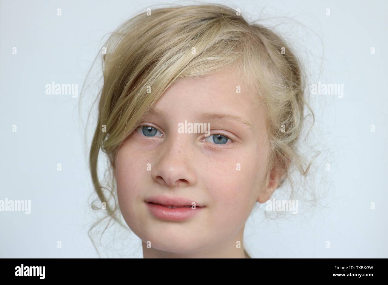 Portrait d'une jeune fille blonde aux yeux bleu maladroitement regardant la caméra sur un fond blanc. Banque D'Images