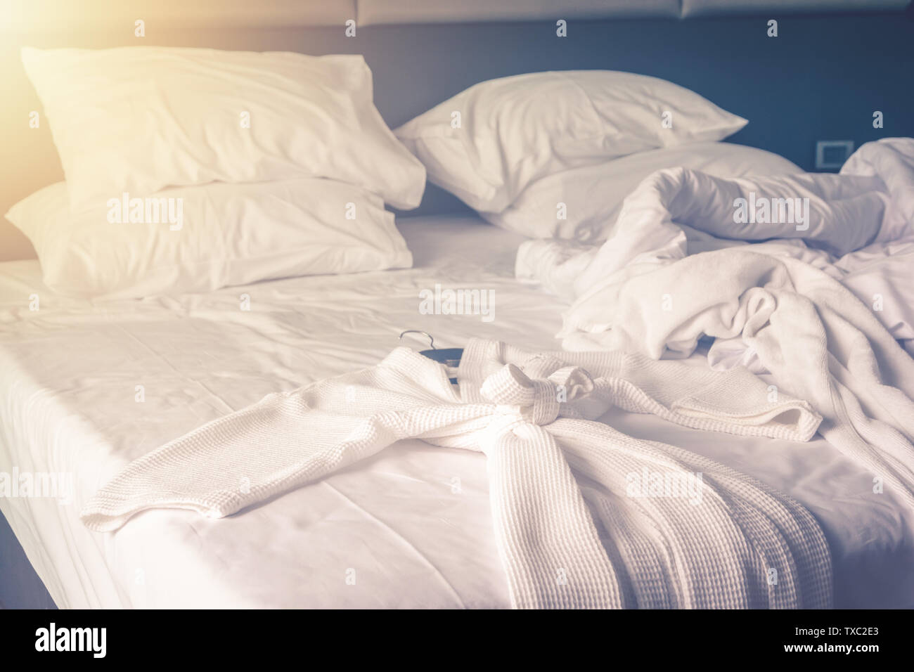 Peignoir sur lit dans chambre confortable après service de literie avec draps et couette avec malpropre de ride dans la chambre à coucher Banque D'Images