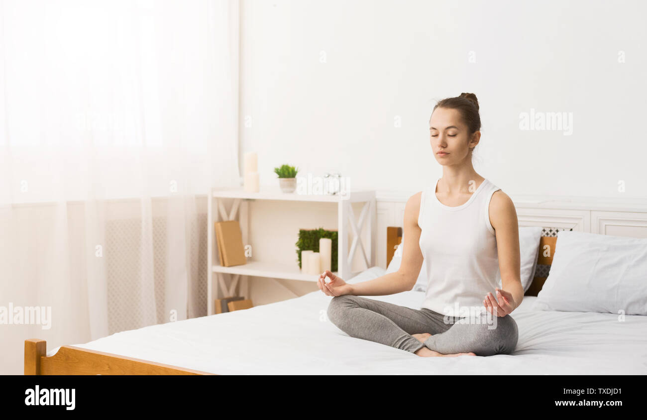 La méditation du matin. Woman Practicing Yoga le matin, assis sur le lit, l'espace libre Banque D'Images