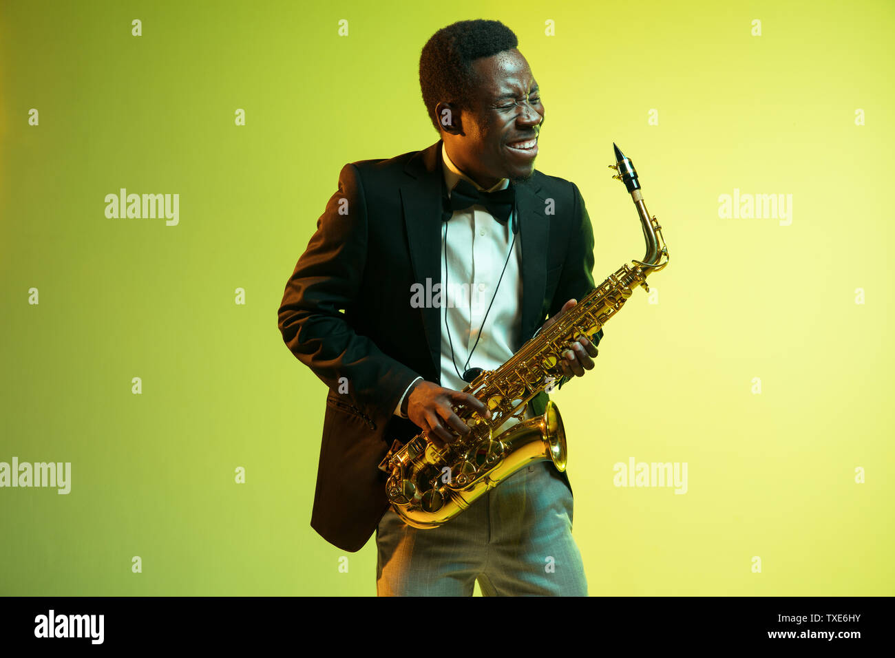 Les jeunes africains-américains musicien de jazz jouant du saxophone sur jaune-vert dégradé fond studio. Concept de la musique, passe-temps, festival. Guy attrayant. improvisation joyeuse Portrait de l'artiste en couleurs. Banque D'Images