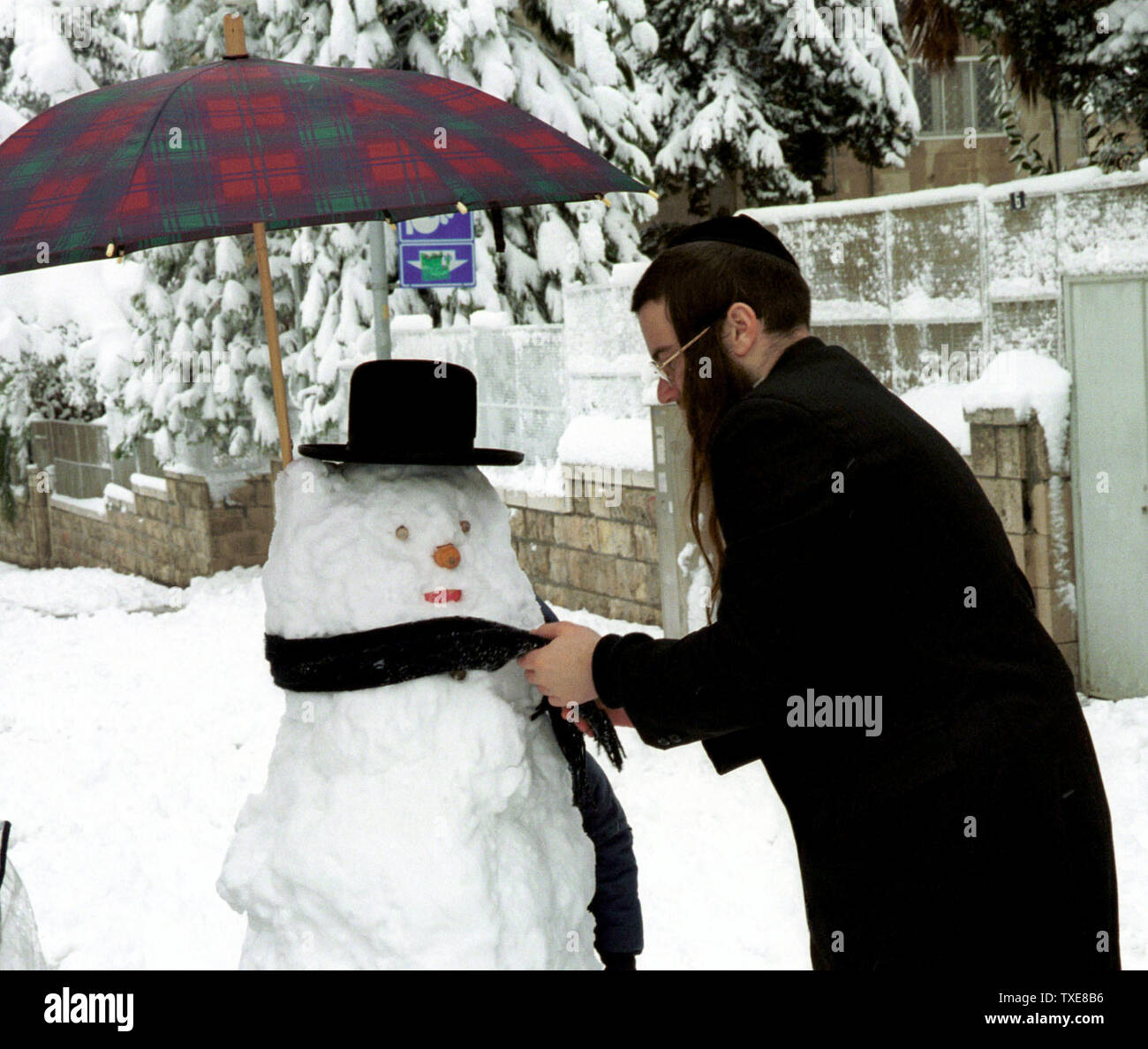 JER2000012806 - 28 janvier 2000 - Jérusalem, Israël : Un Juif ultra-orthodoxes met la touche finale à un bonhomme à Jérusalem au cours d'une tempête de neige inhabituelle qui a laissé 15 centimètres de neige au sol, le 28 janvier. La neige a également diminué pour la première fois en un demi-siècle dans le nord du désert du Néguev et de la Galilée et du Golan dans les régions où les villes ont été coupées à cause des routes fermées et des arbres tombés. jr/dh/Debbie Hill UPI Banque D'Images