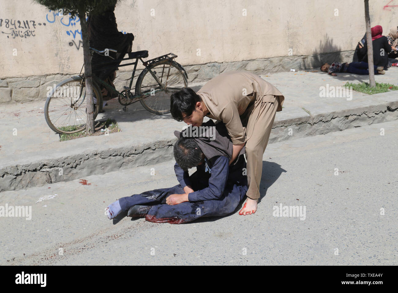 Un citoyen afghan tente d'aider la victime dans sur le site de l'attentat suicide à l'extérieur d'un centre d'enregistrement des électeurs à Kaboul le 22 avril 2018. Un kamikaze s'est fait exploser dans une foule à l'extérieur d'un centre d'inscription des électeurs dans la capitale afghane Kaboul, tuant 48 personnes et en blessant au moins 100 dans la dernière attaque sur les centres. Les assauts de souligner les inquiétudes croissantes au sujet de la sécurité à l'approche des élections législatives prévues pour le 20 octobre. Banque D'Images