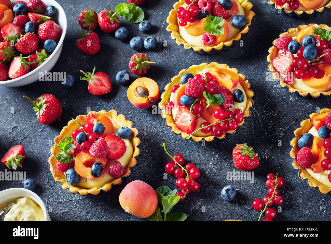 Close-up de l'été tartelettes au citron crème anglaise crémeux garni de framboises, abricots, de bleuet, de fraise, de groseille rouge et de menthe fraîche sur Banque D'Images