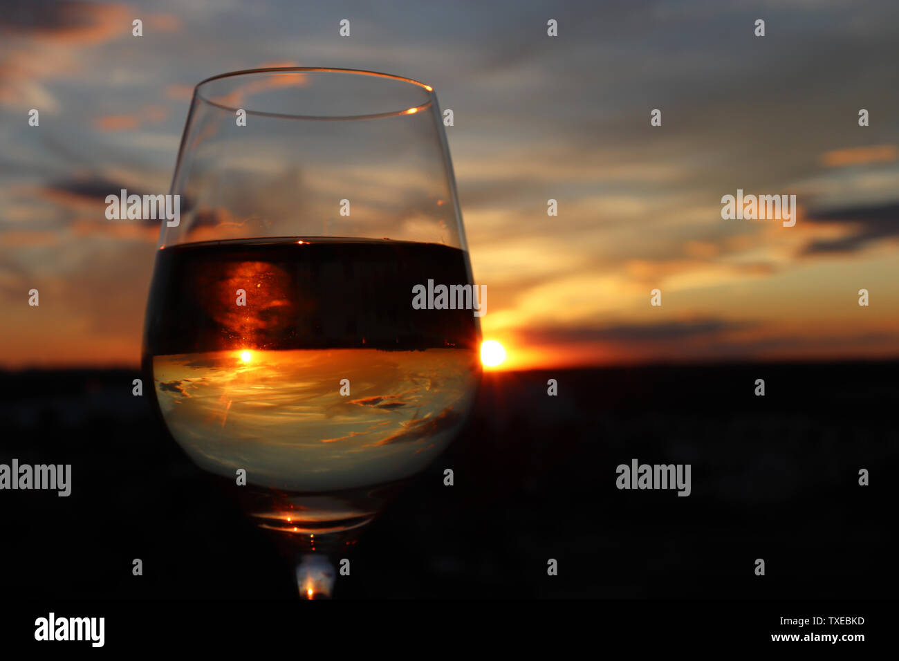 Verre à vin blanc sur fond coucher de soleil magnifique, et le ciel se reflètent dans l'alcool boire. Concept de soirée de célébration, de resort Banque D'Images