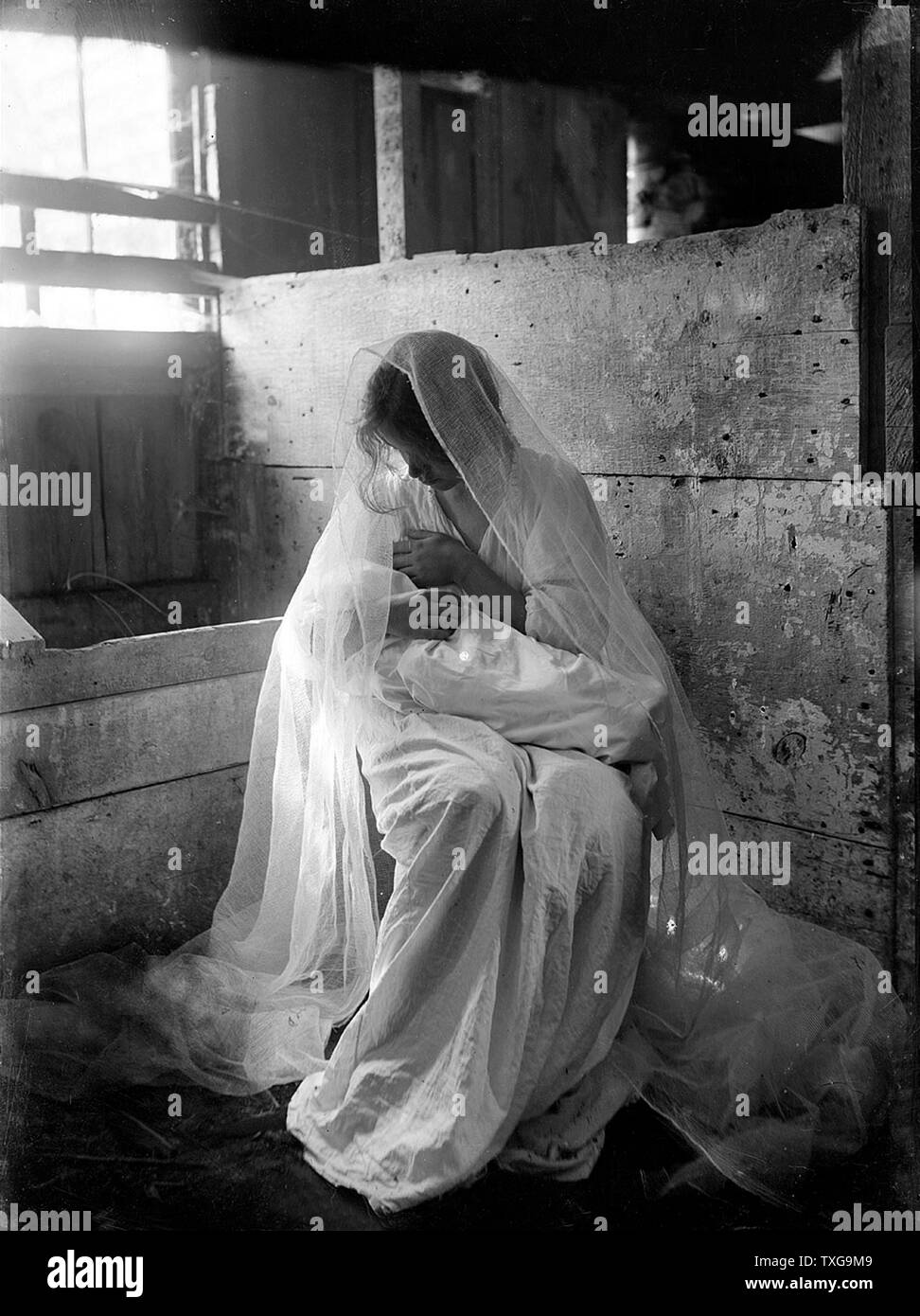 Gertrude Käsebier école américaine. La Crèche - Girl in white tenant un enfant emmailloté posées dans un décrochage avec une crèche. Banque D'Images