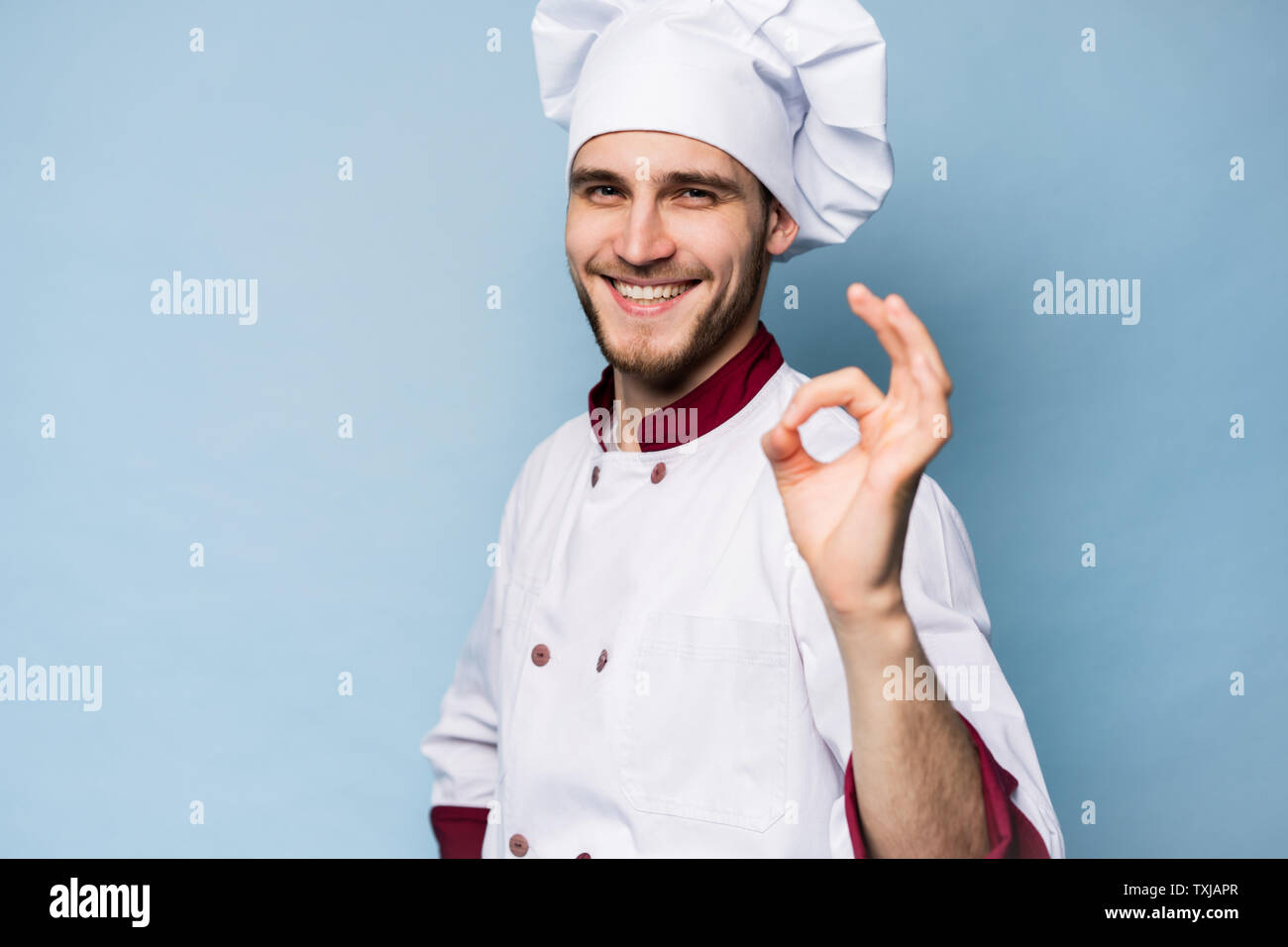 Professionnel positif homme heureux savoureux chef showing ok sign isolé sur bleu clair. Banque D'Images
